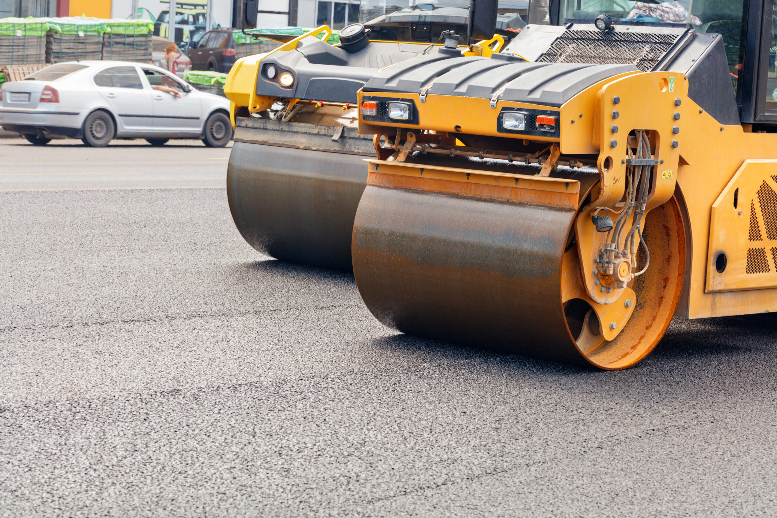 The metal cylinders of yellow road vibratory rollers compacting the fresh asphalt on a road construction site